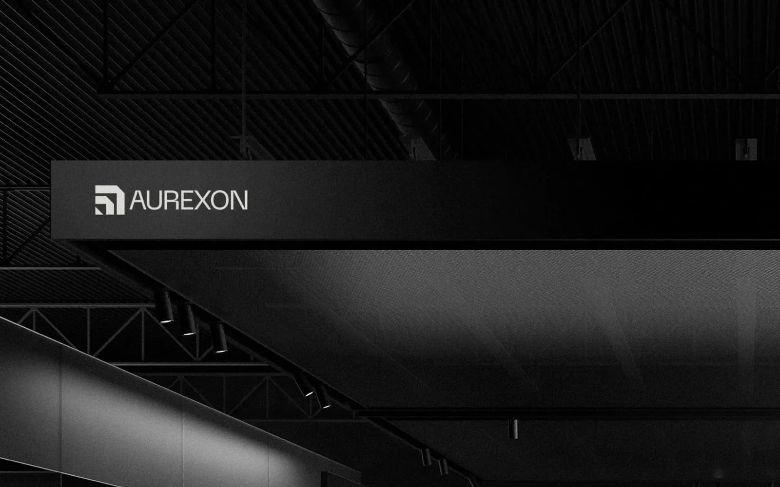 An illuminated Aurexon sign on a long black steel canopy beam inside an industrial building, lit from below by a row of track lights.