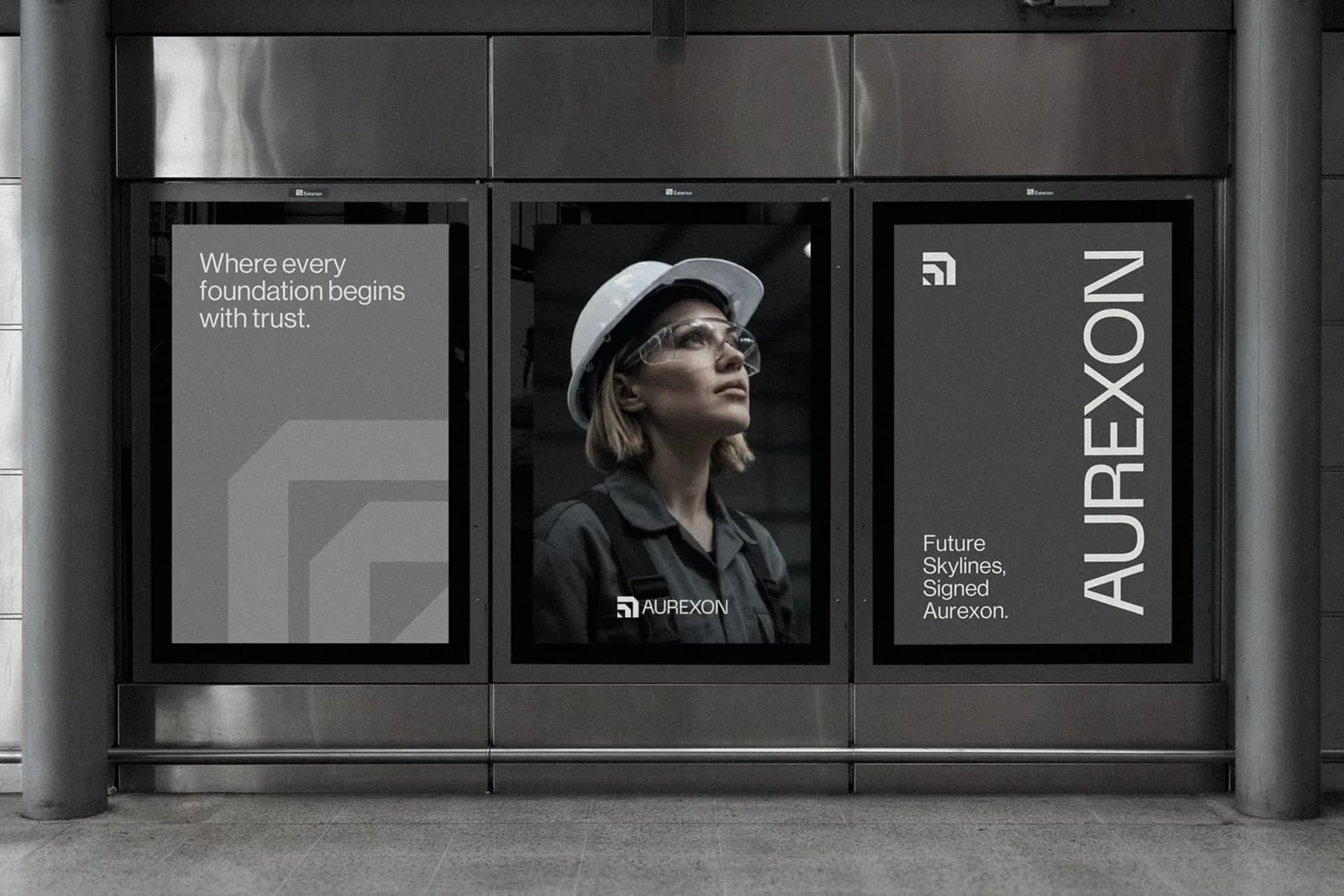 Three Aurexon posters in a steel-framed transit shelter: the line “Where every foundation begins with trust” over a large grey symbol, a portrait of an engineer in a white hard hat and safety glasses, and the wordmark set vertically beside “Future skylines, signed Aurexon”